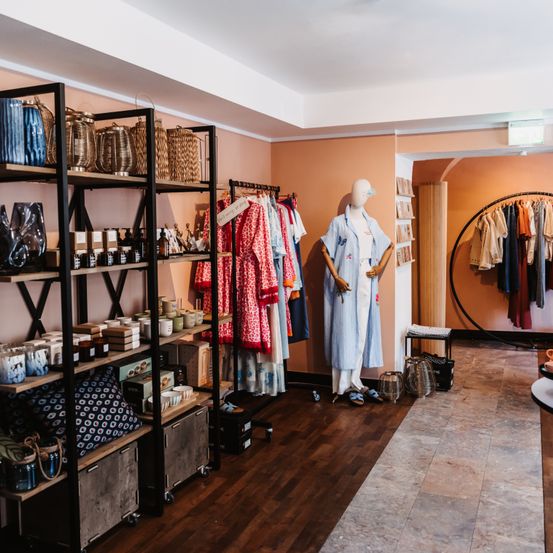 Ein Boutique-Interieur mit Holzböden, Regalen voller Dekorationsartikel und einer Puppe in traditioneller Kleidung.