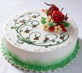 Ein weißer Kuchen mit grünen Blumendesigns und roten Rosendekorationen auf der Oberseite, auf einer weißen Oberfläche platziert.