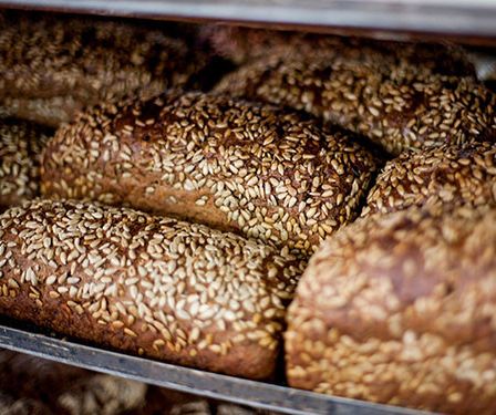 Ein Nahaufnahme von mehreren Brotlaiben mit Sesamkörnern auf einem Metalltablett, wahrscheinlich in einer Bäckerei.