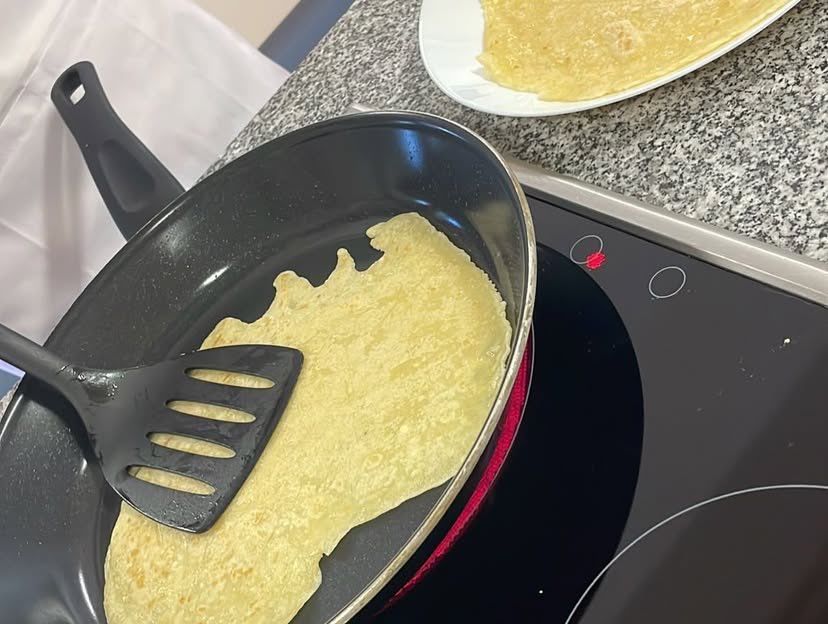 Eine Bratpfanne hält einen fast gekochten Omelett auf einem Herd. Ein Spatel ruht an der Seite. Ein Teller mit einem gekochten Omelett steht auf der Arbeitsplatte.