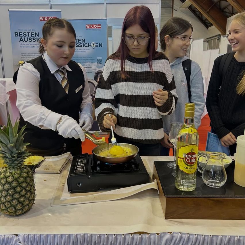 Vier Frauen stehen an einem Kochstation mit Ananas und einer Flasche Havana Club Rum. Eine Frau kocht, eine andere beobachtet aufmerksam, und zwei weitere stehen dahinter.