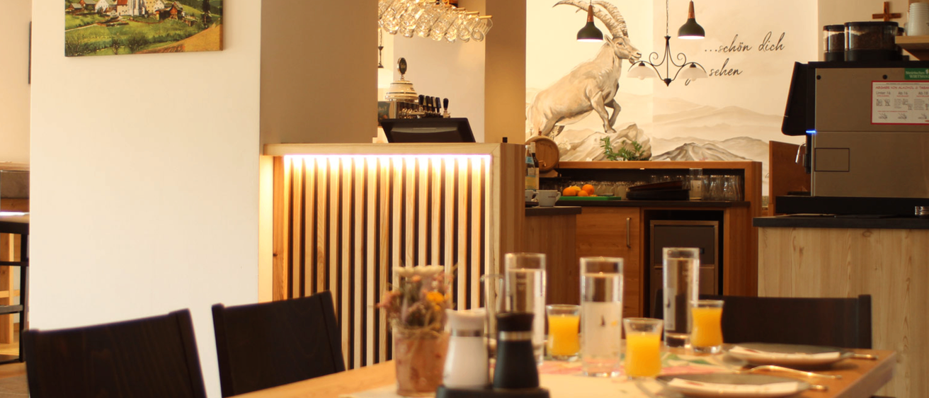 Ein Restaurant-Interieur mit einer Ziegen-Wandmalerei, einem Tisch mit Gläsern und einer Vase mit Blumen.