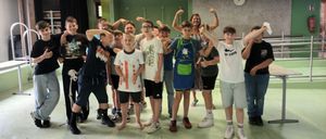 Eine Gruppe junger Jungen und eine Frau posieren für ein Foto in einem Raum mit grünen Wänden. Einige von ihnen tragen Schürzen und Turnschuhe.