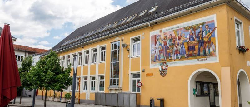 Ein gelbes Gebäude mit Solarpanelen auf dem Dach, das eine große Wandmalerei mit Menschen in traditioneller Kleidung und Musikinstrumenten zeigt.