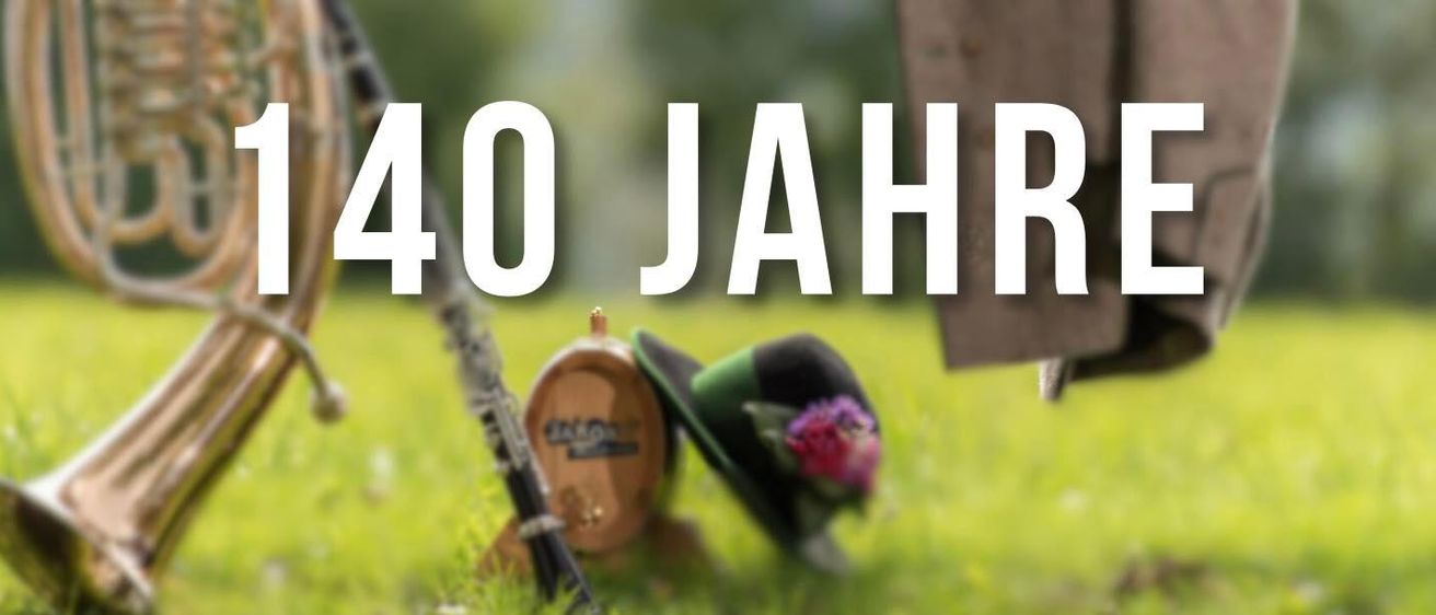 Das Bild zeigt die Worte '40 Jahre' in Weiß vor einem grünen Hintergrund, begleitet von einer Klarinette, einem Fass, einem Hut und einer Blume.