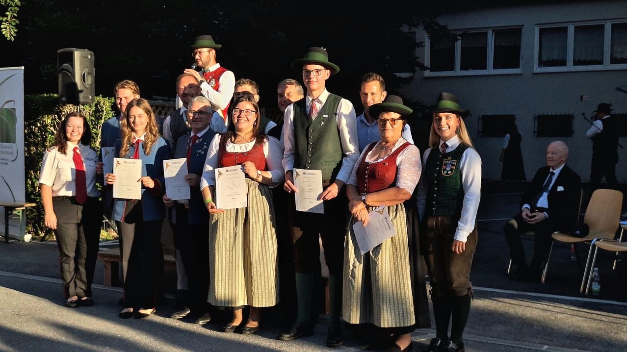 A group of people dressed in traditional attire, holding certificates, standing in a line and smiling for a photo.