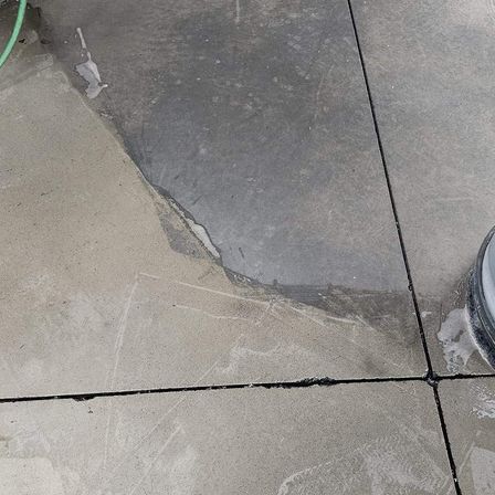 Eine Nahaufnahme eines Betonbodens mit einem feuchten, grauen Bereich und einem grünen Schlauch auf der linken Seite.