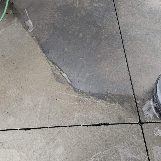 Eine Nahaufnahme eines Betonbodens mit einem feuchten, grauen Bereich und einem grünen Schlauch auf der linken Seite.