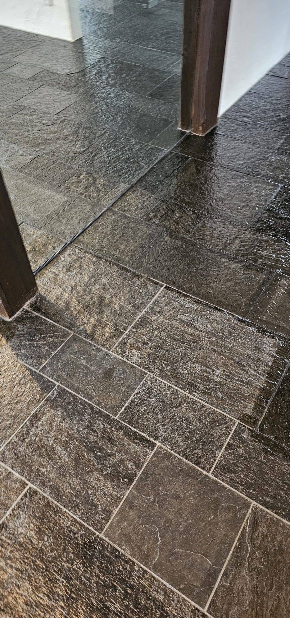 A close-up view of a tiled floor with a wet, shiny surface and a wooden border.