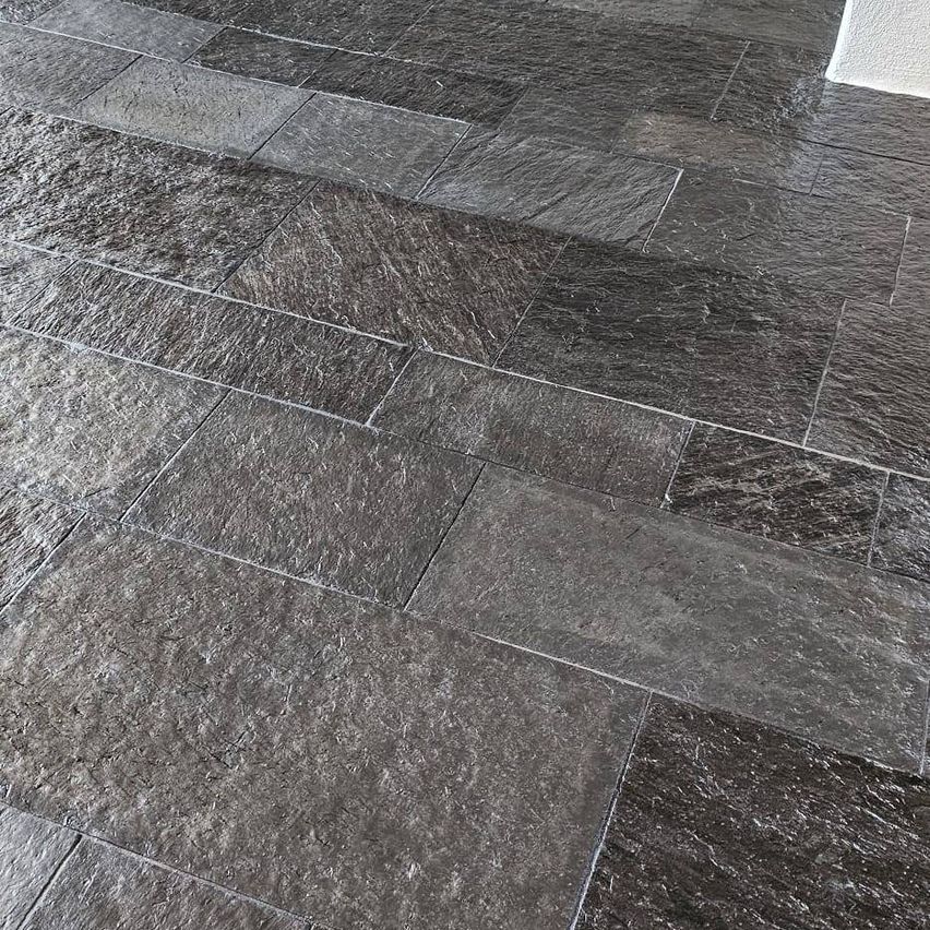 Close-up view of a modern, sleek, and polished black stone tile flooring with a subtle texture and reflective surface.