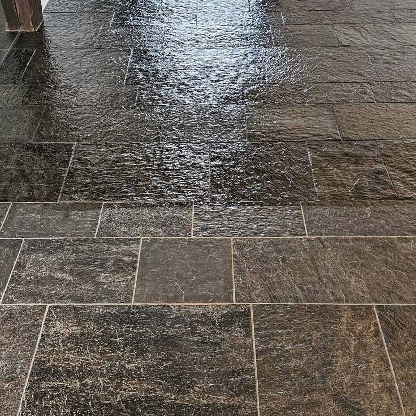 A close-up view of a wet, dark granite tile floor with water droplets and reflections.