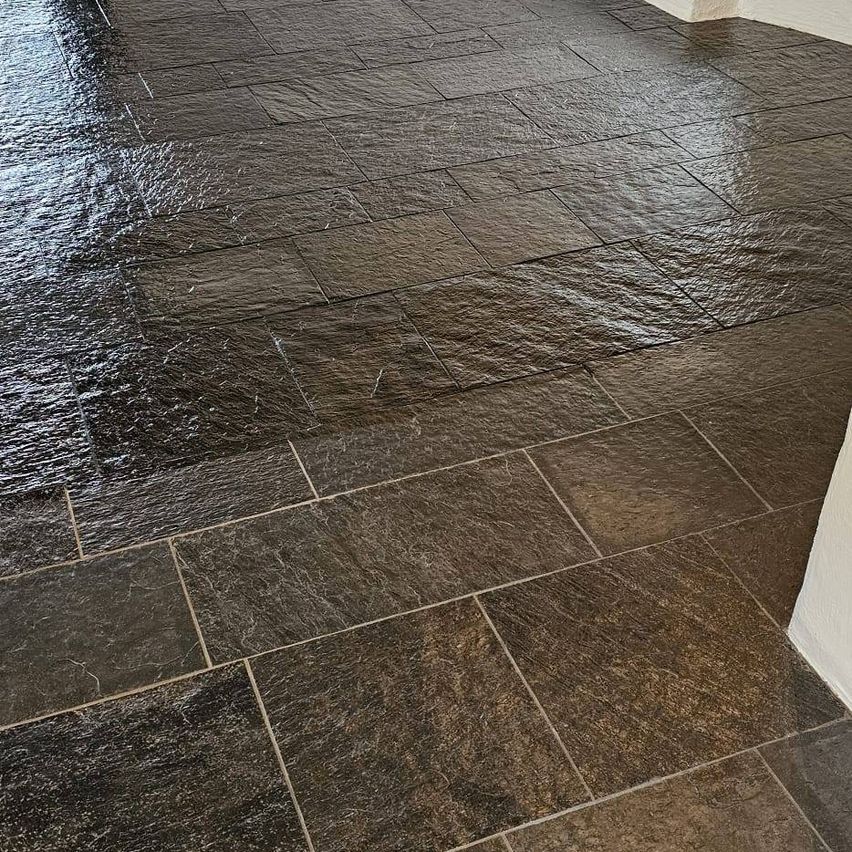 A close-up view of a dark brown stone tile floor with a slightly glossy finish and visible grout lines.