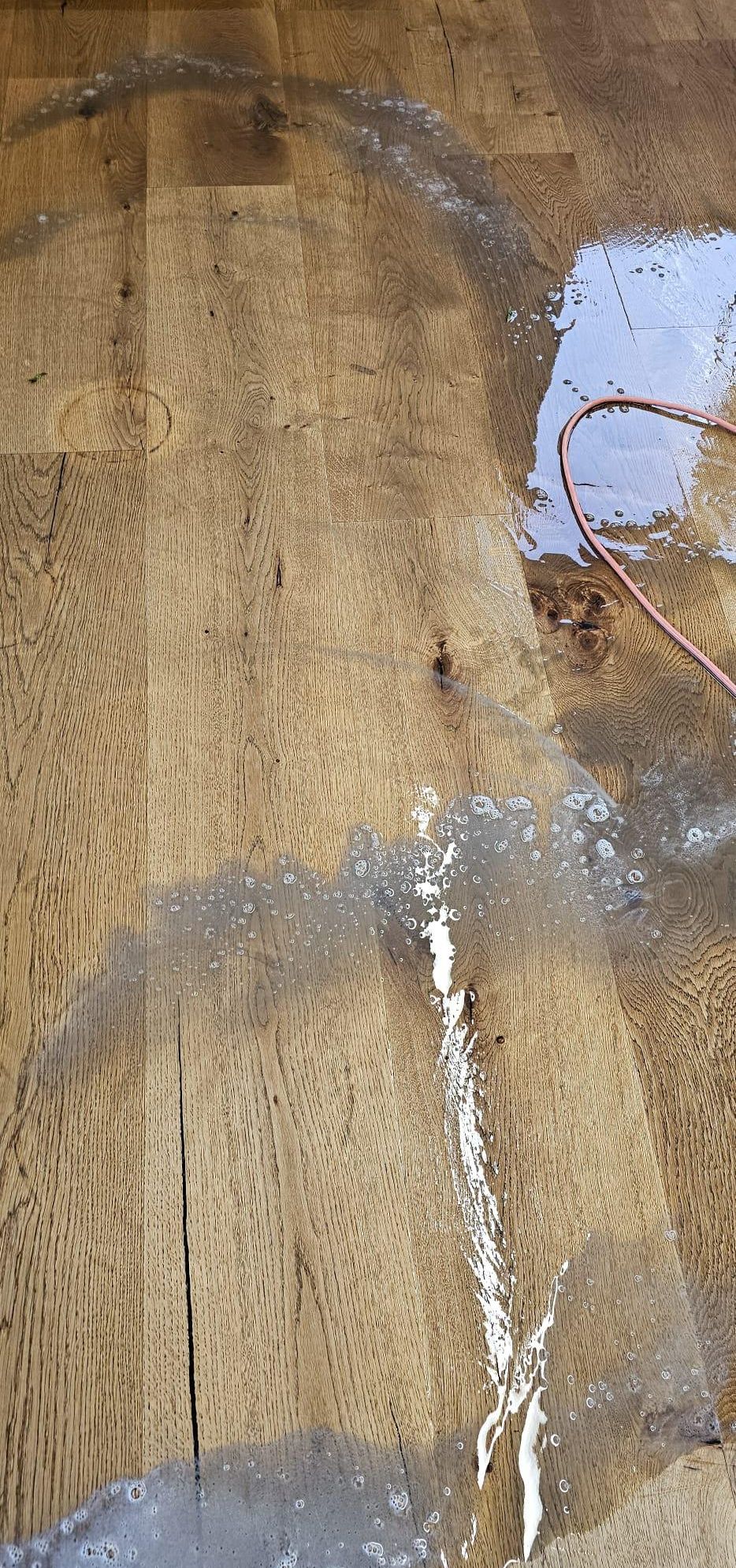 Eine Nahaufnahme eines Holzbodens mit Wasser und Reinigungslösung darauf verteilt. Der Boden hat ein natürliches Maserungsmuster.