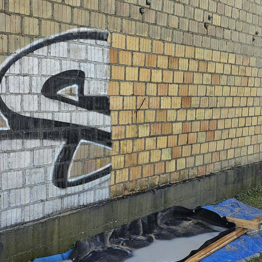 Eine Ziegelwand mit schwarzer Graffiti auf der linken Seite und einer gelben Ziegelwand auf der rechten Seite. Ein blauer Planen liegt auf dem Boden mit etwas Flüssigkeit darauf.
