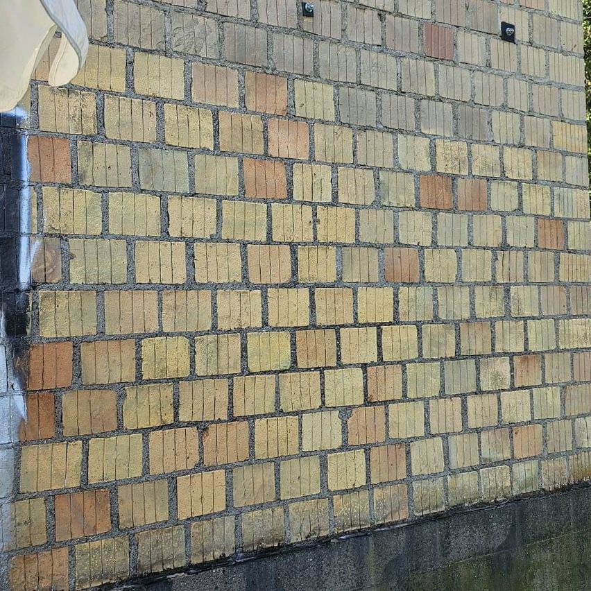 Eine Nahaufnahme einer Ziegelmauer mit verschiedenen Braun- und Gelbtönen, einige Ziegel scheinen abgenutzt, und es sind zwei schwarze Vorrichtungen an der Wand befestigt.