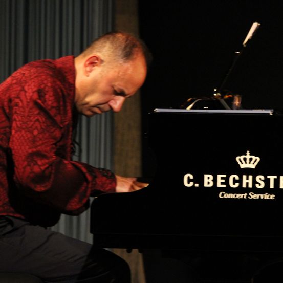 Ein Mann sitzt an einem schwarzen C. Bechstein Klavier, die Augen geschlossen, während er leidenschaftlich eine Melodie spielt.