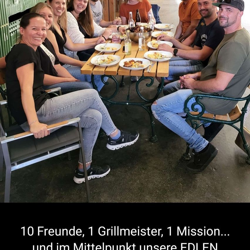 Eine Gruppe von Menschen, die um einen Tisch herumsitzen, der mit Essen und Getränken gefüllt ist, lächeln und für ein Foto posieren. Der Text auf dem Bild lautet '10 Freunde, 1 Grillmeister, 1 Mission...'