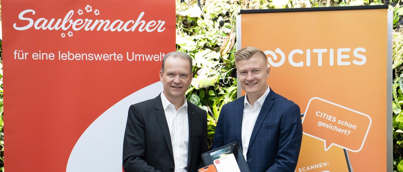 Zwei Männer in Anzügen stehen vor einem Banner, lächeln und halten ein Tablet und ein Smartphone. Das Banner zeigt einen QR-Code und das Wort 'CITI'.
