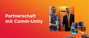 A man in a blue vest and jeans holding a wine glass, smiling and standing beside another person holding a glass.