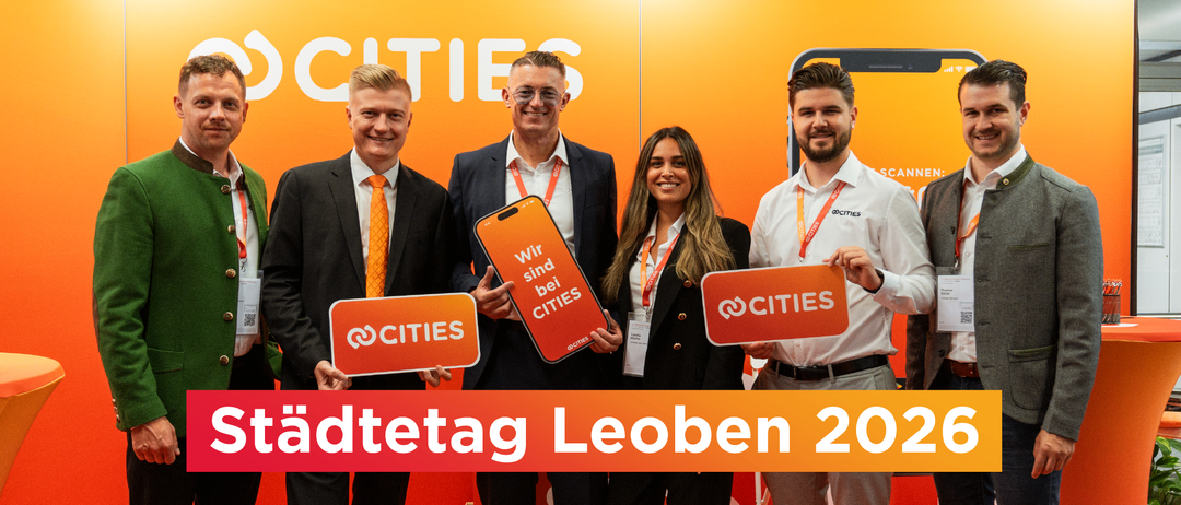 Vier lächelnde Fachleute, zwei Männer und zwei Frauen, stehen hinter orangefarbenen Schildern, auf denen @CITIES und @CITIES sind bei CITIES steht. Der Hintergrund ist orange mit großem Text.