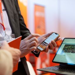 Ein Mann hält ein Telefon mit einer Karte auf dem Bildschirm. Er steht vor einem Laptop mit einer angezeigten Karte.