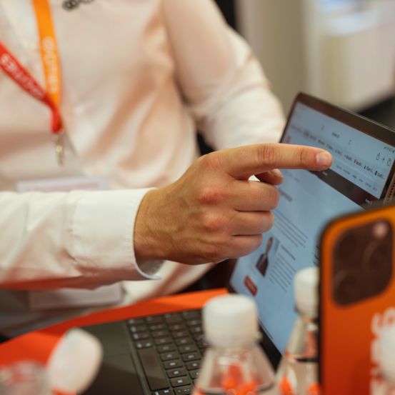 Eine Person in einem weißen Hemd und mit Ausweis benutzt einen Laptop mit Touchscreen und zeigt mit dem Finger auf den Bildschirm.