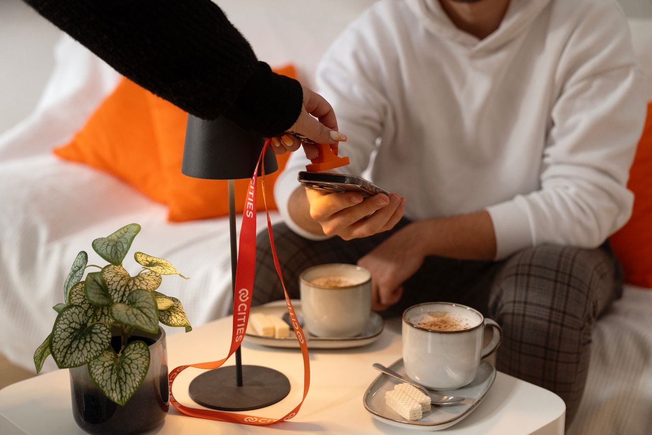 Ein Mann und eine Frau sitzen auf einer Couch. Sie halten ein Telefon und einen Schlüsselanhänger, und auf dem Tisch steht eine Tasse Kaffee und ein Teller mit Keksen.
