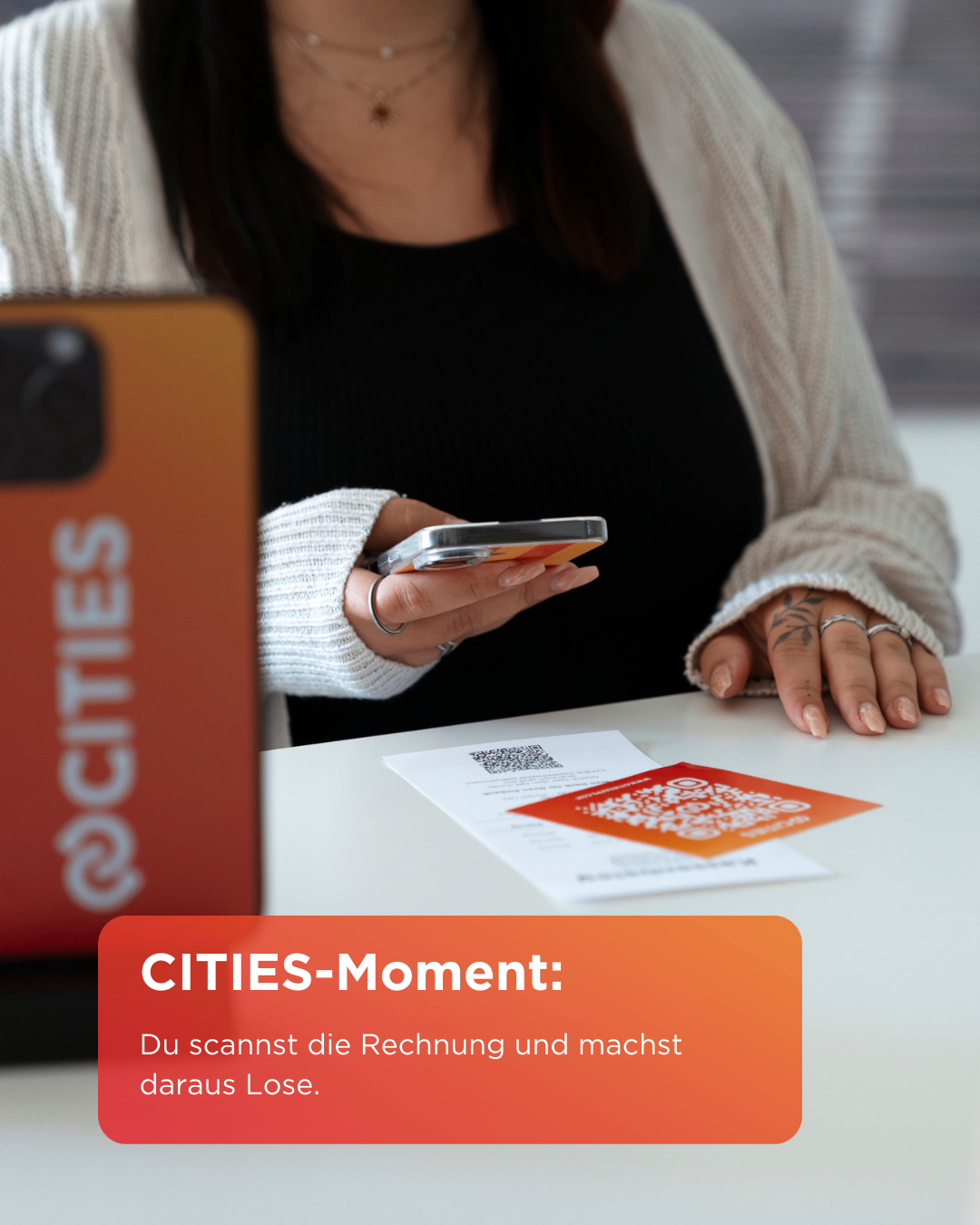 Eine Frau hält ein Smartphone und scannt einen QR-Code. Eine Werbung für Cities ist sichtbar. Der Hinweis lautet: 'Du scannst die Rechnung und machst sie verschwinden.'