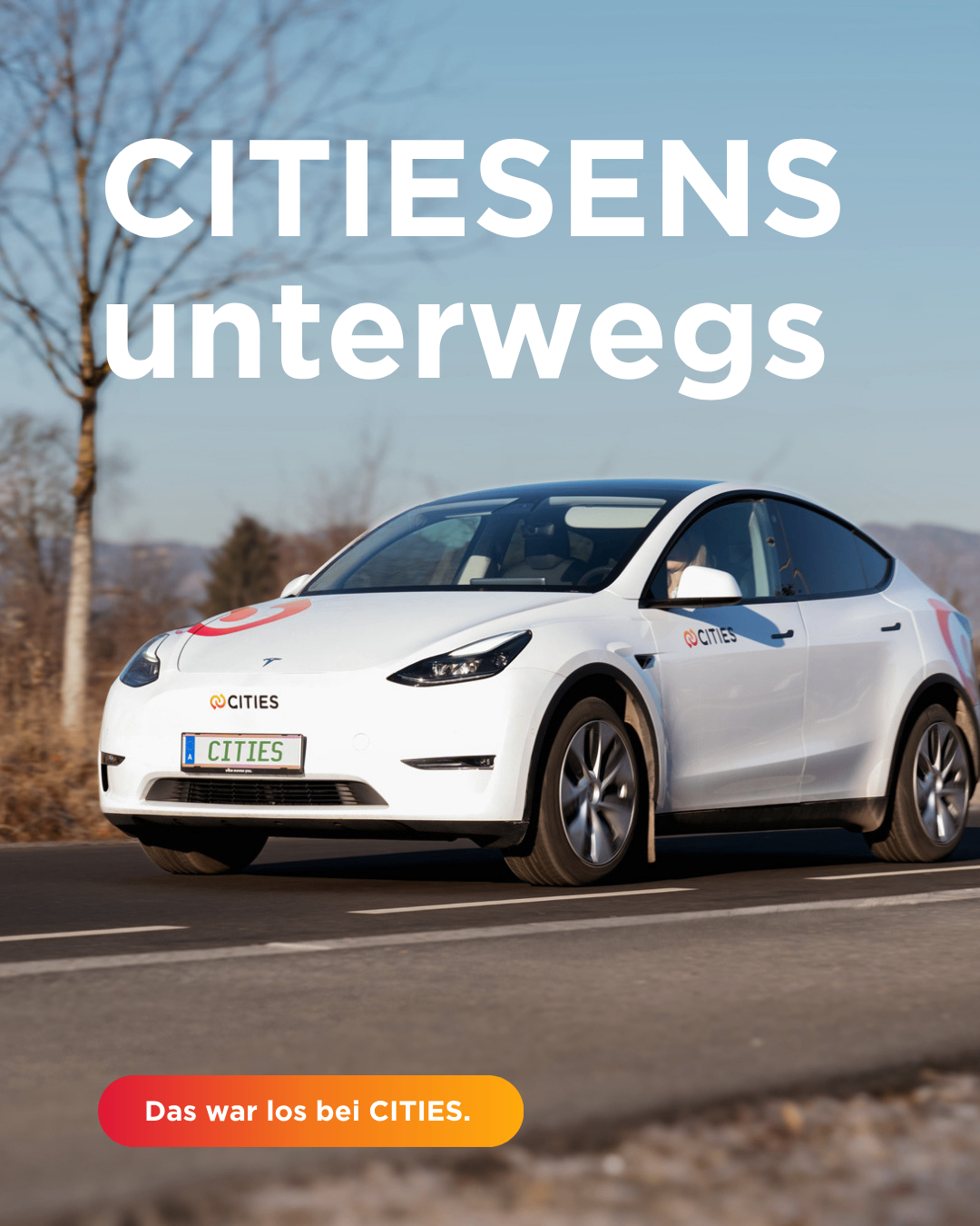 Ein weißer Elektrowagen mit dem Wort Cities vorne und an der Seite fährt auf einer Straße. Er ist auf einer Straße mit einem Baum und Bergen im Hintergrund.