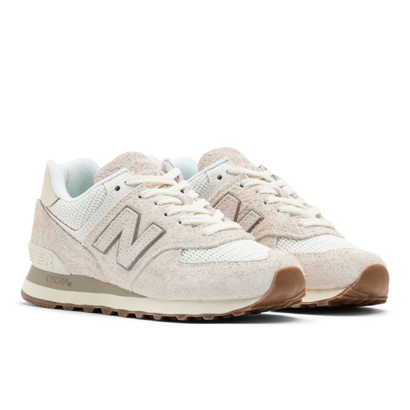New Balance 574 Wildleder-Sneaker in Weiß und Beige mit braunen Sohlen und grauem N-Logo an der Seite.