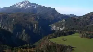 Ein hochgelegener Luftblick auf eine Berglandschaft mit schneebedecktem Gipfel, üppigen grünen Tälern und dichtem Wald.