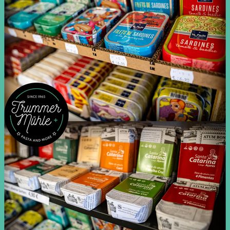 Ein Geschäft zeigt eine Vielzahl verpackter Lebensmittelprodukte, darunter Dosen Sardellen und Packungen von Santa Catarina Produkten, mit sichtbaren Preisschildern.