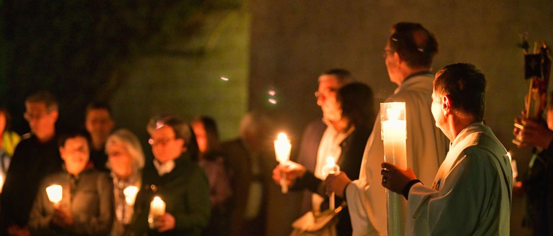 Eine Gruppe von Menschen hält brennende Kerzen in der Dunkelheit, vielleicht bei einer Gedenkfeier.