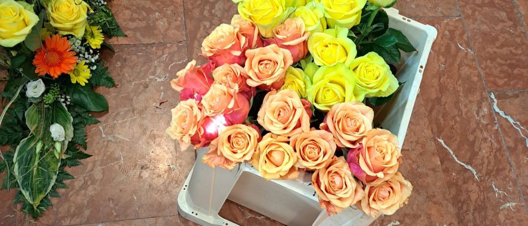 Eine weiße Box auf einem Marmorboden enthält einen Strauß Rosen. Die Rosen sind in Gelb- und Orangetönen. In der Nähe ist ein weiterer Strauß mit gemischten Blumen.