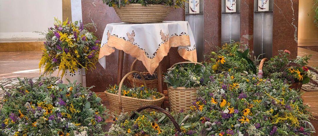 Eine Blumendekoration in einer Kirche mit Körben und Kerzen auf dem Altar. Bunte Blumen sind in Weidenkörben auf dem Boden arrangiert.