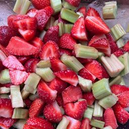 Eine Schüssel mit gemischten Erdbeeren und Rhabarberstücken, wobei die Erdbeeren in Scheiben und der Rhabarber in Stäbchen geschnitten wurden, mit Zuckerkristallen bestreut.
