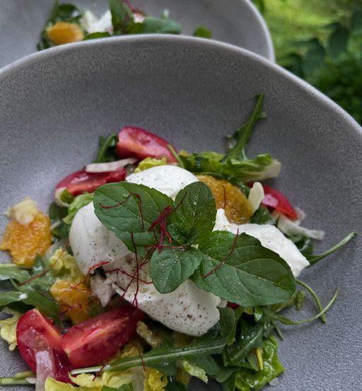 Eine Schüssel Salat mit Salat, Tomaten und Käse, garniert mit Minzblättern und Orangenscheiben.