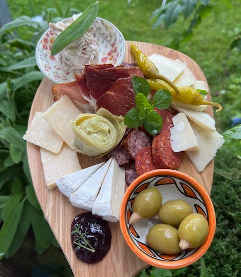 Ein Holzbrett mit verschiedenen Lebensmitteln wie Käse, Fleisch, Oliven und Kräutern.