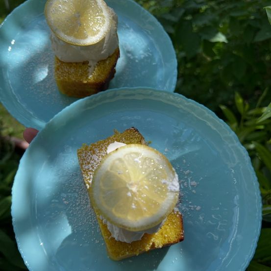 Zwei Zitronenkuchen mit weißer Creme auf hellblauen Tellern, garniert mit Zitronenscheiben und Puderzucker, im Freien.