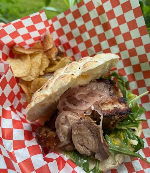 Ein Sandwich mit Fleisch, Zwiebeln und Grünzeug in einer roten und weißen karierten Papiertüte mit Kartoffelchips.