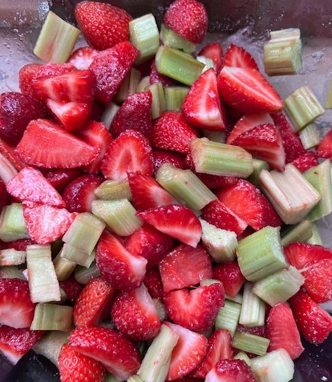 Eine Schüssel mit gehackten Erdbeeren und Rhabarberstücken auf einer Holzoberfläche. Die Erdbeeren sind rot mit einigen sichtbaren Samen.