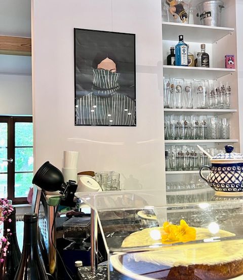 Ein Raum mit einem Tresen, einem Kuchen in einer Glasvitrine, Flaschen und einem Bild an der Wand.