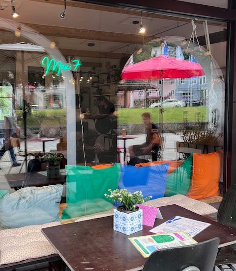 Ein gemütliches Café mit farbenfrohen Sitzsäcken, einem Tisch mit einer Pflanze und einer Person, die unter einem roten Regenschirm sitzt.