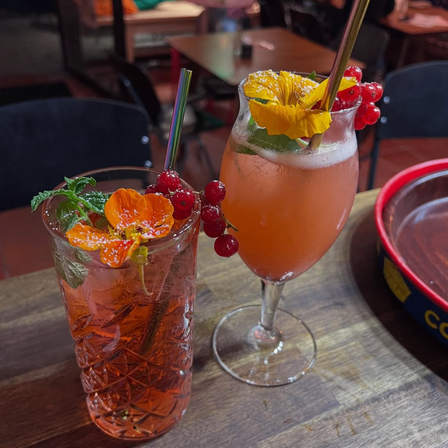 Zwei Getränke auf einem Holztisch in einem Restaurant mit orangefarbenen Blumen und roten Beeren als Garnierung.