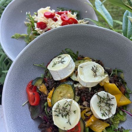Ein Salatschüssel mit gemischtem Gemüse und Käse, garniert mit Kräutern, auf einem Tisch mit einem weiteren Salat im Hintergrund.