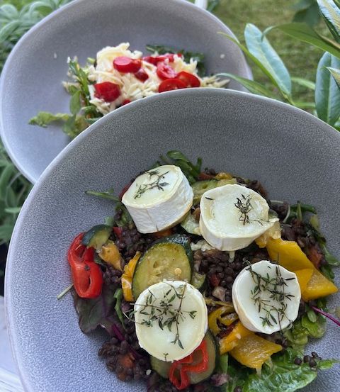 Ein Salatschüssel mit gemischtem Gemüse und Käse, garniert mit Kräutern, auf einem Tisch mit einem weiteren Salat im Hintergrund.