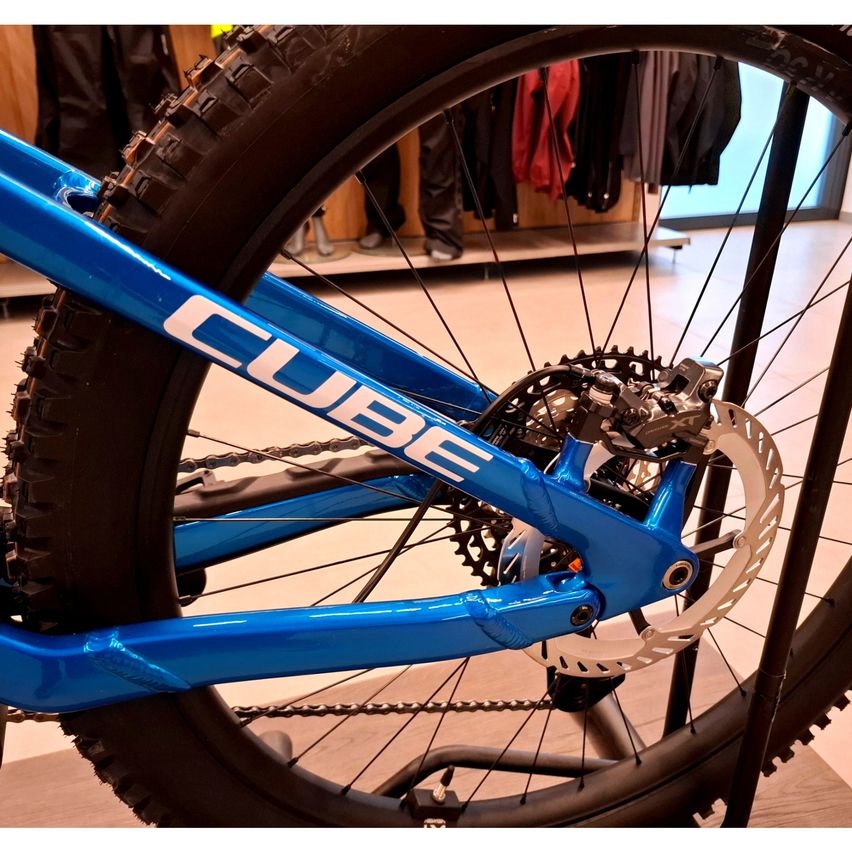 Eine Nahaufnahme eines blauen Cube-Mountainbikes mit schwarzen Reifen und silbernen Kettenblättern, ausgestellt in einem Geschäft.