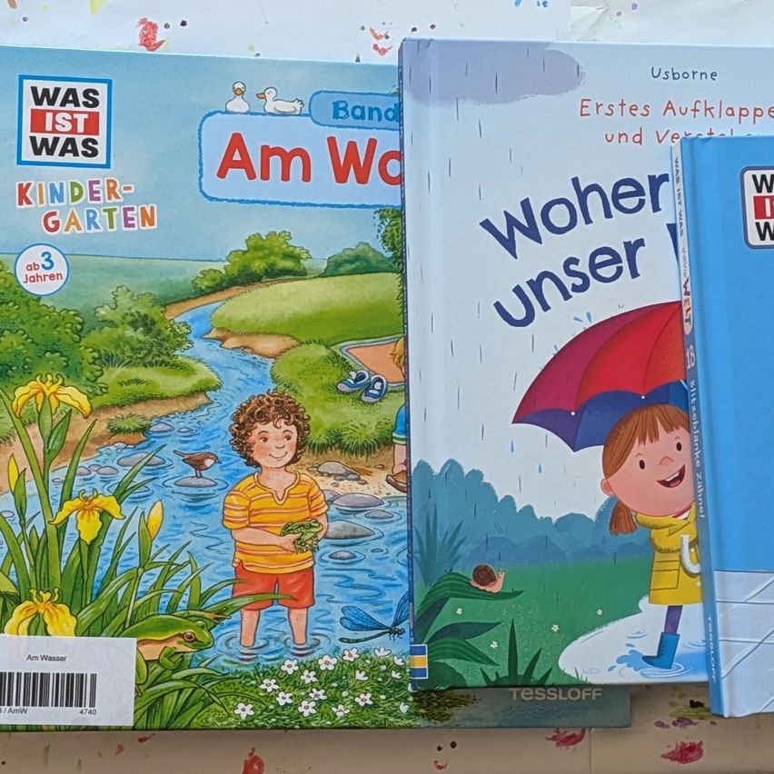 Drei Kinderbücher, die zusammengestapelt sind. Ein Buch zeigt ein Kind am Fluss, ein anderes zeigt ein Kind mit einem Regenschirm und das dritte hat eine Ente auf dem Cover.