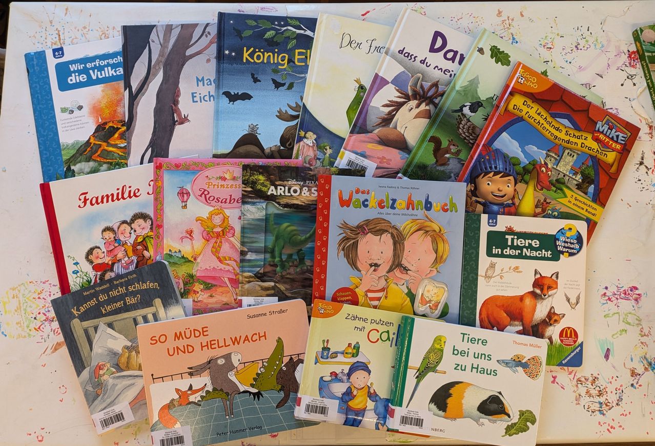 A collection of children's books arranged on a table. Titles include 'Das Wackelzahnbuch', 'Tiere bei uns zu Haus', and 'So Müde und Hellwach'. Each book has a distinct cover design with illustrations and text.