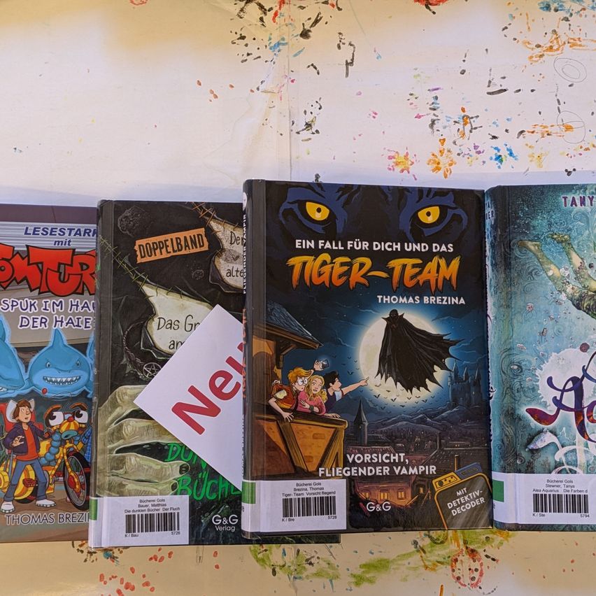 Eine Sammlung von Büchern auf weißem Hintergrund. Das mittlere Buch zeigt eine Katze und einen Mond. Das Wort 'Neu' ist auf einem weißen Papier geschrieben.